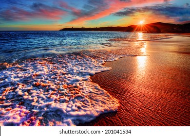 Brilliant vacation destination beach sunrise with colorful sand bright sea foam pink clouds and distant cliffs