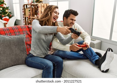 Jonge Spaanse paar glimlachend gelukkig zittend op de bank videospel thuis spelen.