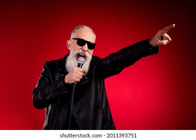 Portret van een aantrekkelijke, vrolijke, populaire grijsharige man die een hit zingt en plezier heeft terwijl hij geïsoleerd over een felrode kleurachtergrond rust