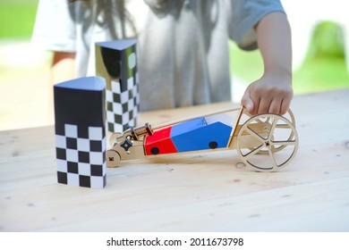 Car race DIY.Wooden vehicle craft.Child assembling racecar in outdoor.Homeschooling learning engineering.Checkered paper on pine wooded table.Design and speed toy.Transportation.