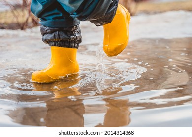 Kaki seorang anak dengan sepatu bot karet menginjak genangan air