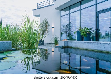 Air di kolam ikan mencerminkan pemandangan dinding kaca rumah modern dan menciptakan suasana yang menenangkan. Gaya hidup di luar kota
