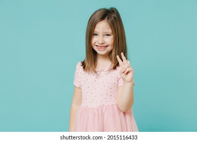 Little funny cute kid girl 5-6 years old wears pink dress show victory v-sign gesture isolated on pastel blue color background child studio portrait. Mother's Day love family people lifestyle concept