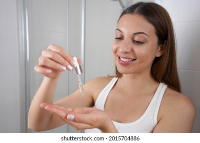 Young Skin Care Routine. Beautiful girl applying a serum moisturizing anti aging antioxidant to her face while holding a pipette in her hand.