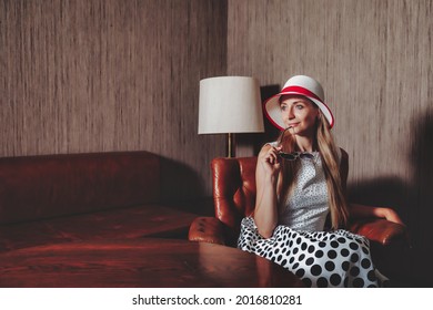 Retrato mujer adulta actriz posando en ropa de estilo retro con gafas de sol en la sala de estar vintage. Mujer con vestido blanco y negro de estilo pin-up con lunares y sombrero. Concepto de moda retro y tendencia