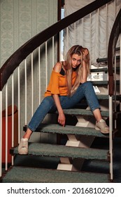Retrato mujer adulta actriz posando en la escalera de casa vestida con ropa de estilo en la sala de estar vintage. Mujer con pelo largo en estilo chaqueta naranja. Concepto de moda retro y moda de tendencia obsoleta