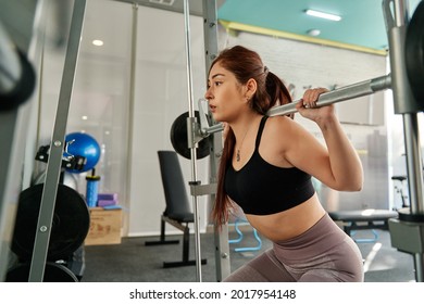 young redheaded woman performing a squat on a smith machine