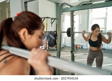 young latina woman performing a squat on a smith machine