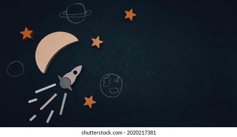 Cohete, luna, estrellas y planetas pintados a la izquierda sobre un fondo negro con espacio para texto a la derecha, vista superior de primer plano.