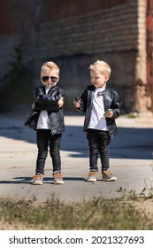 Zwillingsbrüder in Lederjacken und Sonnenbrillen. Zwei identische blonde Jungen vor dem verlassenen Gebäude. Kinder in einem coolen und mutigen Bild für ein Fotoshooting. Kinder sehen aus wie Prominente oder Models.