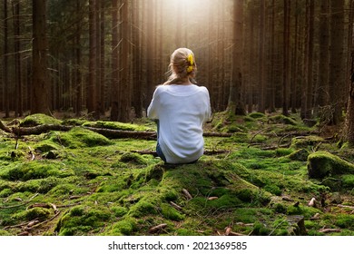 Blond beautiful woman sitting in moss forest meditating and enjoys the silence and beauty of nature.