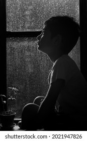 Karachi, Pakistan - 10 Juli 2021: Bidikan siluet Kid duduk di jendela dan hujan di luar. melihat melalui jendela