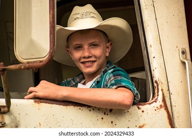 Een jonge plattelandsjongen met een cowboyhoed kijkt uit het raam van een oude roestige vintage werktruck Een gelukkige, glimlachende tiener op de voorbank van een oude boerderijtruck Een jonge man rijdt in een oude vrachtwagen