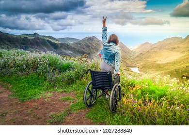 No rendirse nunca. Vista trasera de una joven discapacitada sentada en silla de ruedas en la cima de la montaña con las manos arriba y mirando el asombroso paisaje natural mientras viaja sola. Día Internacional de la Discapacidad