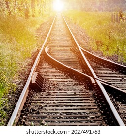 Vías de ferrocarril, con un interruptor en primer plano, que conduce al infinito con la luz roja del sol naciente en el centro del fondo.