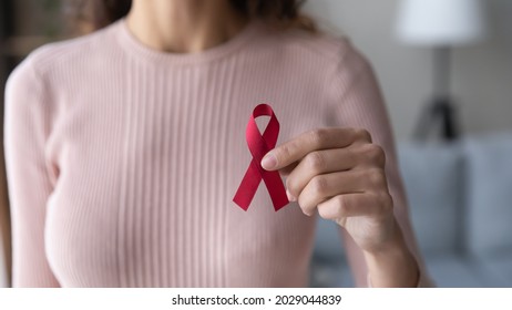 Close up view female volunteer holding red ribbon in hands. Symbol of fighting against HIV, showing support to people with AIDS, concept of awareness, regular medical check up promotion, healthcare