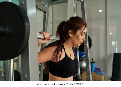 serious young latina woman performing squats on smith machine at gym