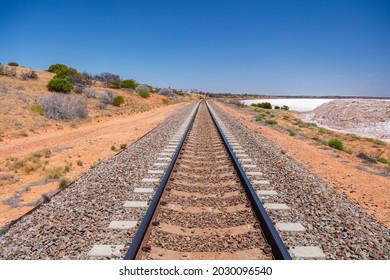 Railroad tracks of the Indian Pacific Railway near the Salt Lake of Lake Heart. Railway across the Australian Outback. Single track railway line through the barren landscape. From Perth to Sydney 