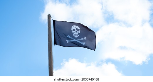 青い空に風になびく黒い海賊の頭蓋骨の旗。海賊行為とハッキングの象徴。