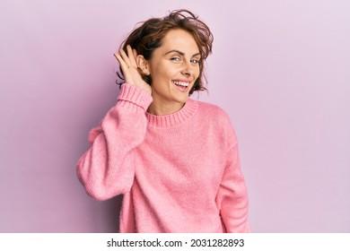 Young brunette woman wearing casual winter sweater smiling with hand over ear listening and hearing to rumor or gossip. deafness concept.