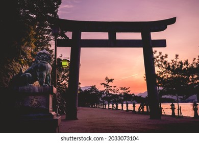 日本の宮島から見た、鳥居、ライオンの彫刻、海に沈む夕日、地平線に山々が見える素晴らしい景色 (日本語のテキストは、島の名前である「厳島」を意味します)