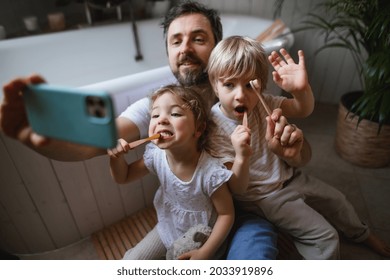 Father with two small children brushing teeth indoors at home, taking selfie.
