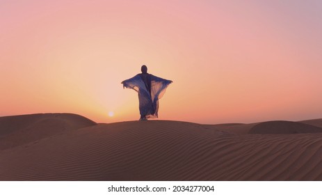Arabische vrouw, gekleed in traditionele kleding van de VAE - abayain die haar handen opsteekt op de zonsondergang in een woestijn.