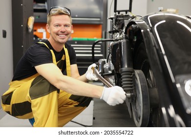 Tânăr reparator în salopete care repara motocicleta în atelier