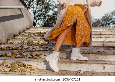 close-up benen in stijlvolle witte laarzen schoeisel van jonge vrouw in gele bedrukte jurk op zonnige herfstdag plezier in straat dragen van modetrend outfit