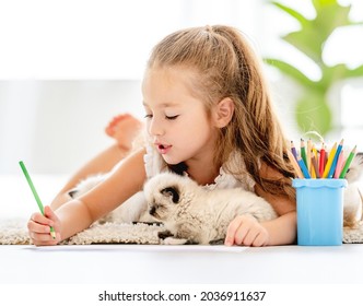 Kind meisje schilderen met ragdoll kittens en liggend op de vloer. Kleine vrouwelijke persoon tekenen met kleurrijke potloden en kattenhuisdieren dicht bij haar thuis