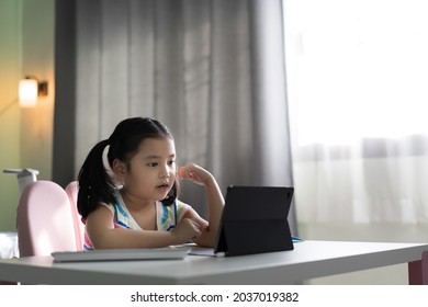 asiatische kinderschülerin zurück zur schule oder kindermädchen e-learning und lesen auf dem computer-tablet-bildschirm per videoanruf oder leute lernen von zu hause aus, indem sie online-kurse auf blöcken und fensterlicht mit warmweißer lampe lernen