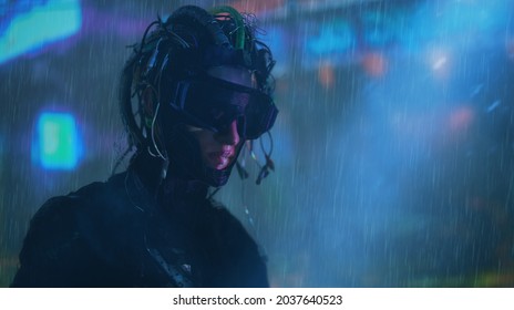 Potret seorang prajurit cyberpunk mengenakan topeng dan dengan kabel di kepalanya berdiri di bawah hujan dalam cahaya neon kota malam. Dunia masa depan. Permainan, realitas maya.