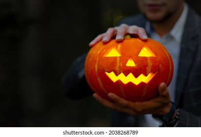 Man in suit holds a carved glowing pumpkin lantern with a creepy face. Halloween concept