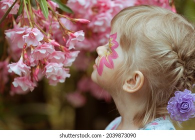 A girl with makeup on her face is sniffing pink flowers.