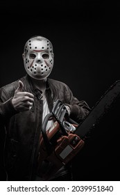 Man in mask with chainsaw posing over dark background