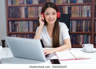 Smiling Asian female wearing headphones using laptop , happy young female listening to favorite music while working online on project, self education .