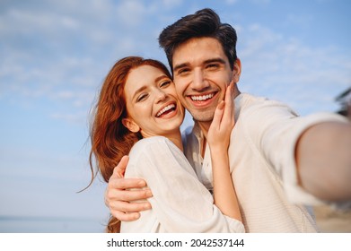 Nahaufnahme zufriedenes, glückliches junges Paar zwei Familienmann Frau 20er Jahre in weißen Kleidern umarmen einander tun Selfie Schuss pov auf dem Handy bei Sonnenaufgang über dem Meer Strand im Freien am Meer im Sommer Tag Sonnenuntergang Abend