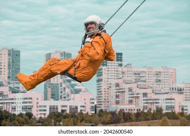 Gelukkig kosmonaut lacht en kijkt naar de camera terwijl hij buiten op de schommel zwaait. Astronaut draagt ​​oranje ruimtepak en helm op een schommel tegen bewolkte hemel.