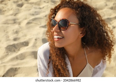 Beautiful African American woman with sunglasses at sandy beach. Sun protection care
