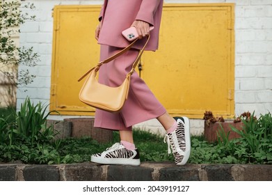 Street Fashion-Elemente: Frau im trendigen Outfit mit rosafarbenem Anzug, Sneakers mit Zebradruck und gelber Kunstlederhandtasche. Kopieren, leerer Platz für Text