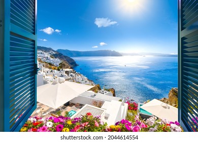 Blick aus einem offenen Fenster mit blauen Fensterläden auf das Ägäische Meer, die Caldera, die Küste und die weiß getünchte Stadt Oia, Santorini, Griechenland.