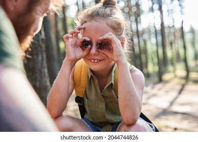 Girl show pine cones on eyes to father in forest