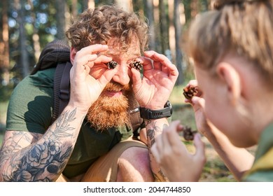 Man show pine cones on eyes to daughter in forest