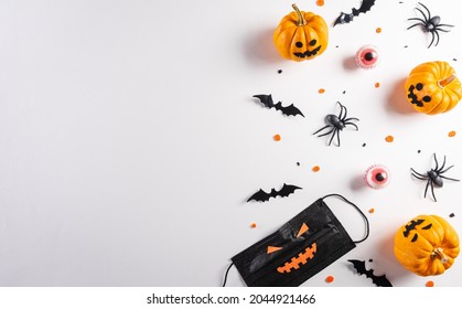 Halloween decorations made from pumpkin, paper bats, medical mask and black spider on white background. Flat lay, top view with copy space for text.