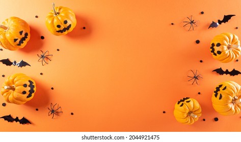 Halloween decorations made from pumpkin, paper bats and black spider on orange background. Flat lay, top view with copy space for text.