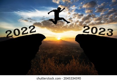 A young man jump between 2022 and 2023 years over the sun and through on the gap of hill  silhouette evening colorful sky. happy new year 2022.