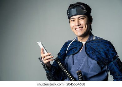 Samurai japonês sorridente, armado, usando um smartphone.