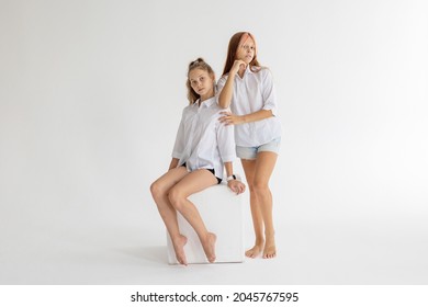 Dos chicas adolescentes artísticas con camisas blancas y pantalones cortos de jeans entrena y divirtiéndose sobre fondo blanco en ejercicio de gimnasia rítmica, deportes profesionales para niños