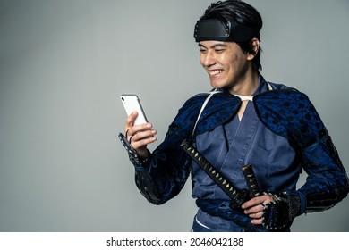 Samurai japonês sorridente, armado, usando um smartphone.