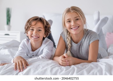 Glückliches Zeitkonzept. Bruder und Schwester liegen morgens im Bett und lächeln in die Kamera. Jungen- und Mädchengeschwister, die entspannend auf dem Bett spielen.